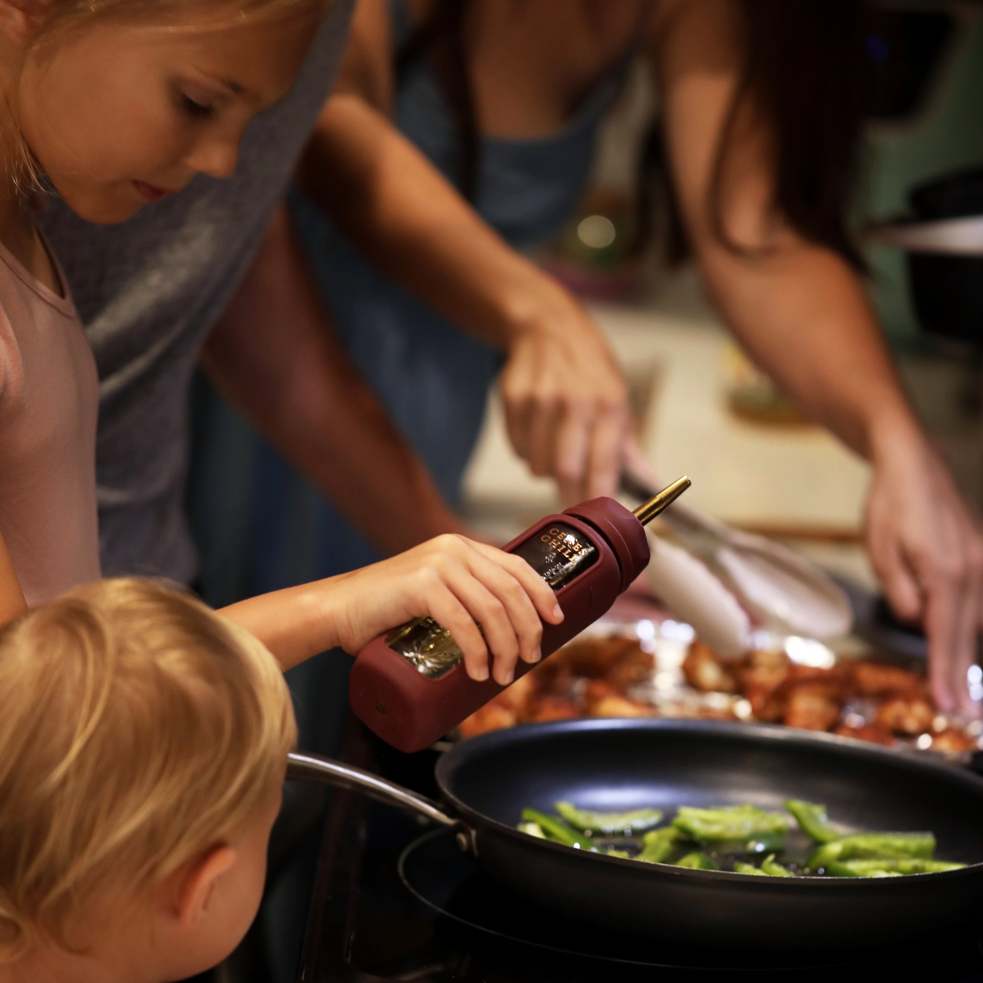 A child using the oil dispenser accessory for the Bloom Bottle in the kitchen while cooking with her family. 