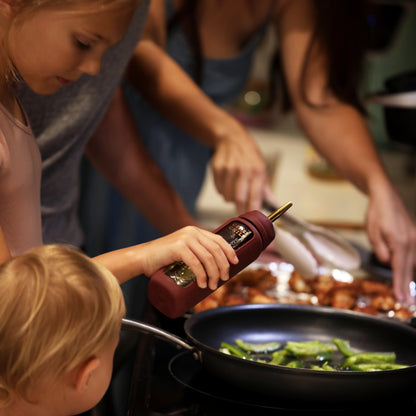 A child using the oil dispenser accessory for the Bloom Bottle in the kitchen while cooking with her family. 