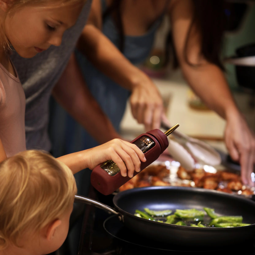 A child using the oil dispenser accessory for the Bloom Bottle in the kitchen while cooking with her family. 