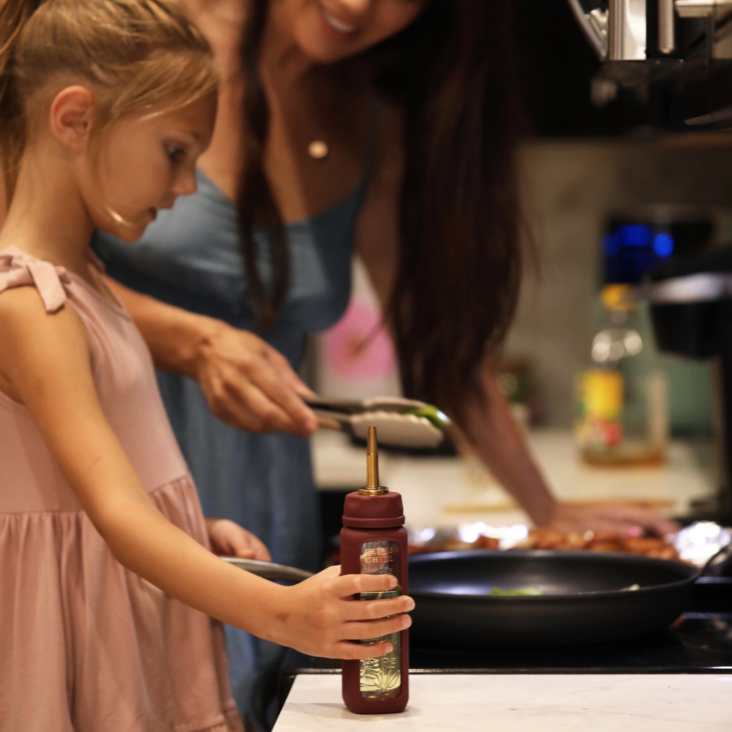 A child, cooking with her mother, using the Bloom Bottle paired with the oil dispenser attachment. 