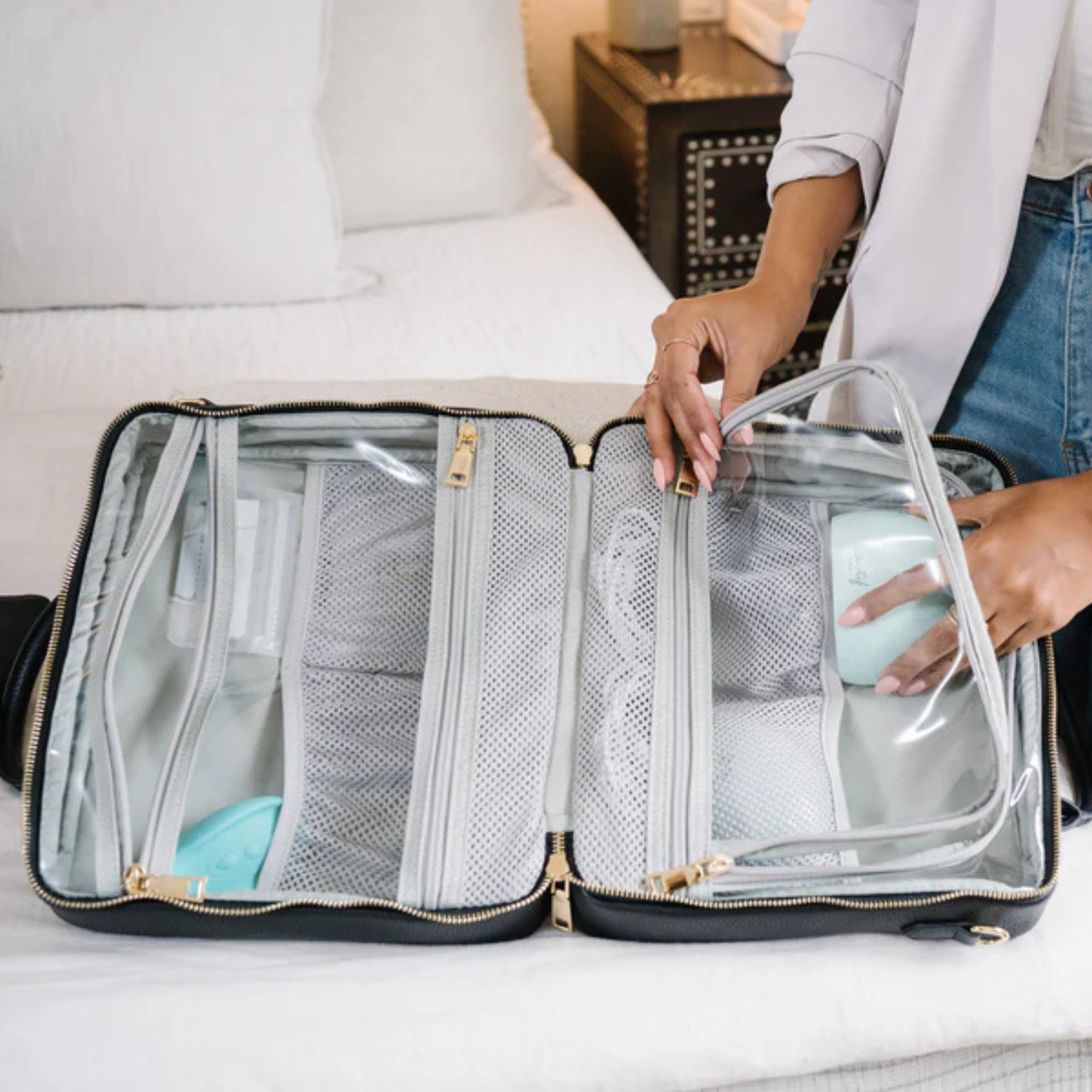 Person packing a clear travel organizer with breast milk storage on a bed.