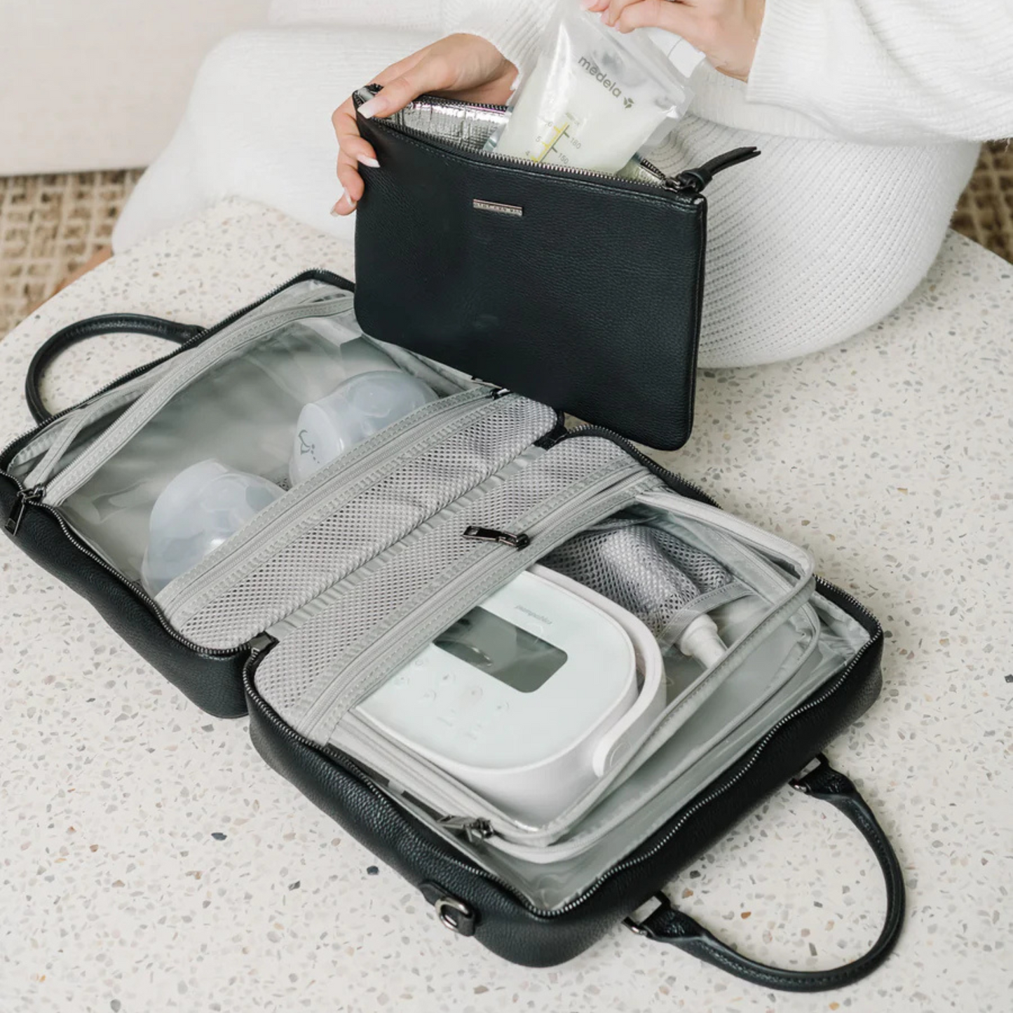 Black travel bag with a breast pump and containers on a light surface