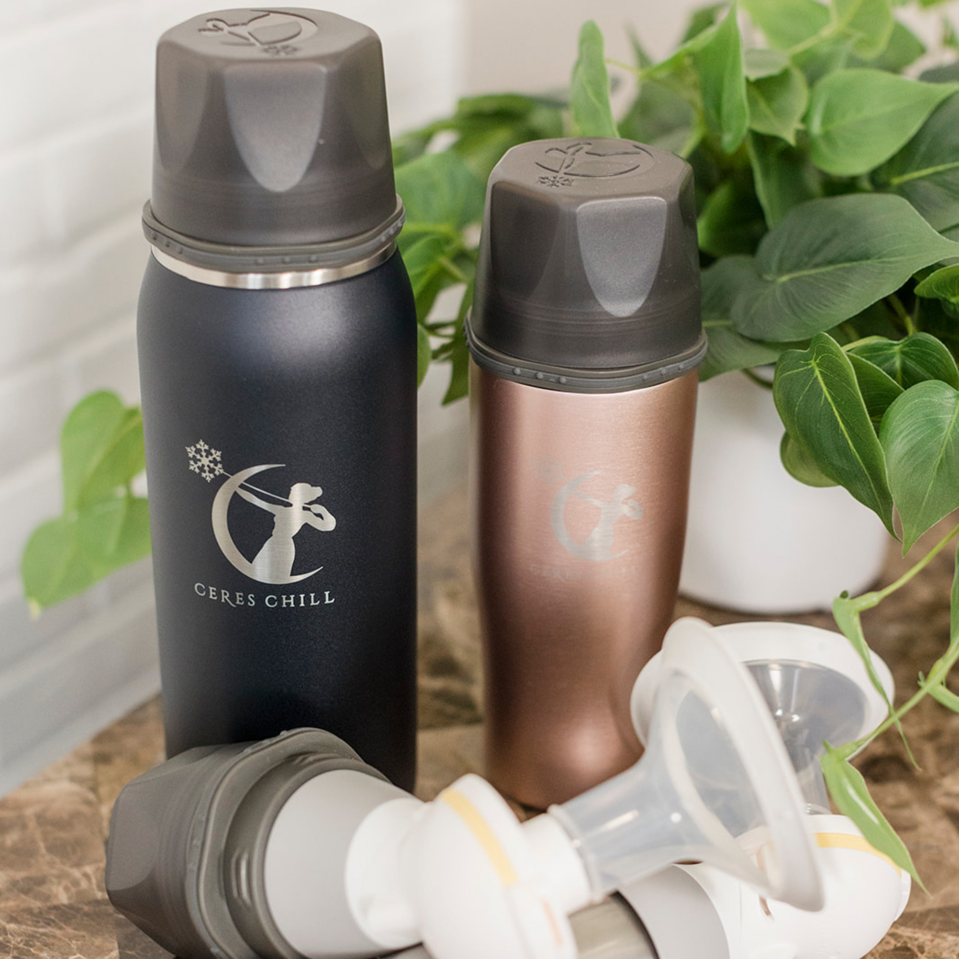 Two insulated Ceres Chill bottles with a logo and a breast pump on a surface with green plants in the background.